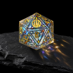 May include: A twenty-sided die featuring a stained-glass inspired design with a translucent, iridescent core. The surface is divided by black lines into geometric shapes, with gold-colored numbers and a gold symbol at the top vertex.