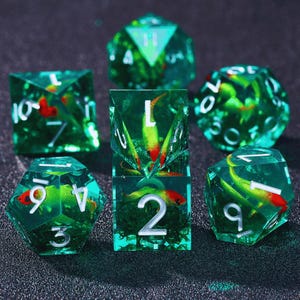 May include: Set of seven green and clear dice with a fish design. The dice are numbered 1 through 6 and have a fish design inside. The dice are made of clear plastic and have a green tint.