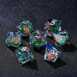 May include: A collection of seven polyhedral dice with a clear, faceted design. Each die features a colorful octopus design suspended within the transparent resin, with green glitter accents. The dice are numbered in white and are suitable for tabletop gaming.