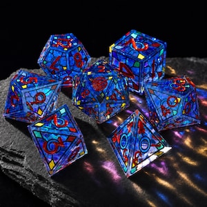 May include: A set of seven polyhedral dice featuring a stained-glass aesthetic with translucent blue and purple panels, black grid lines, and vibrant red numbers. The dice have a glossy finish and reflect light, creating colorful patterns on the surface.
