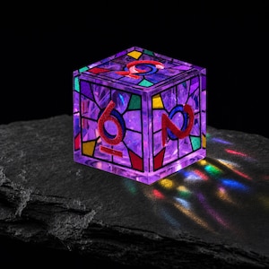 May include: A translucent purple six-sided die featuring a stained-glass pattern with red, yellow, green, and blue geometric segments. The numbers are embossed in a bold red font, and the die casts colorful light reflections onto the surface below.
