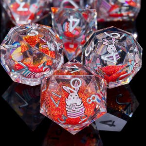 May include: A set of six clear, iridescent dice with a red glitter fill and bunny illustrations. The dice are numbered 1-6 and have a pastel color scheme.