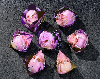 May include: Set of seven polyhedral dice with a skull design encased in translucent purple resin. The dice have silver numbering and are arranged on a dark surface. Ideal for tabletop gaming.