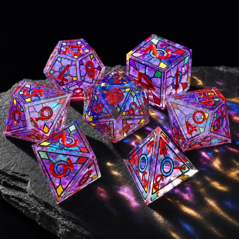 May include: A set of seven polyhedral dice featuring a stained-glass aesthetic with translucent purple, blue, and green panels outlined in black. Each die has bright red numbers embossed on the faces, creating a vibrant, multi-faceted appearance.