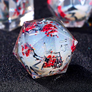May include: A clear, multi-sided die with a floral design. The die features red flowers and black branches set against a white and glittery background. The numbers are in a silver colour.