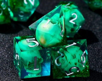 May include: A set of green and clear resin dice with silver numbering. The dice have a unique design with embedded green and yellow elements, creating a layered effect. The dice are displayed on a dark surface.