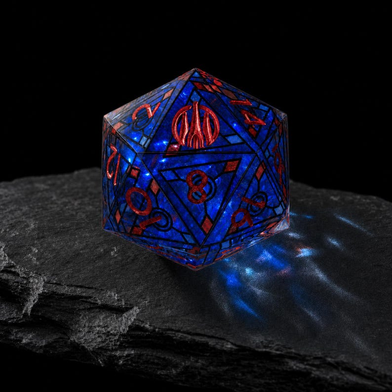 May include: A twenty-sided die featuring a deep blue translucent body with a stained glass-like grid pattern. The numbers are engraved in a metallic red finish, with a prominent red symbol replacing the number twenty on the top face.