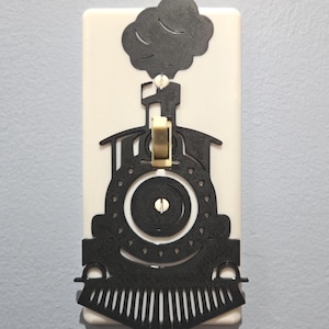 May include: A white light switch cover with a black silhouette of a train engine with smoke coming out of the chimney. The train engine is facing forward and has a large wheel in the center. The light switch is in the center of the train engine.