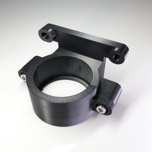 Könnte beinhalten: Eine schwarze, 3D-gedruckte Halterung mit einer kreisförmigen Öffnung und einem rechteckigen oberen Abschnitt. Die Halterung hat zwei Befestigungslöcher oben und zwei an den Seiten, die mit silbernen Schrauben befestigt sind. Das Objekt ist für die Montage konzipiert.