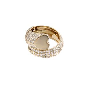 May include: A gold ring with a heart-shaped design. The ring is encrusted with small, clear gemstones, creating a sparkling effect. The heart is a solid, polished gold. The ring is set against a white background.