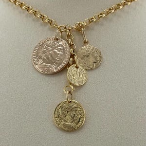 May include: Gold necklace with multiple coin pendants. The chain has a link design, and the pendants are circular and of different sizes. Each pendant shows a detailed profile of a person, possibly a historical figure.