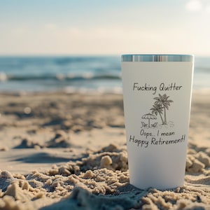 May include: A white tumbler with a silver rim, featuring the text "Fucking Quitter" above a palm tree and beach scene, followed by "Oops... I mean Happy Retirement!" The tumbler is set on a sandy beach with the ocean in the background.