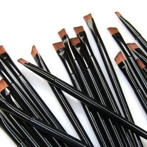 May include: A set of black angled eyeliner brushes with brown bristles. The brushes are arranged in a pile, with the handles pointing in different directions.
