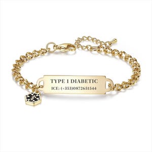 May include: Gold-toned medical ID bracelet. The bracelet features a rectangular plate engraved with "TYPE 1 DIABETIC" and an ICE contact number. A small charm with a medical symbol hangs from the bracelet. The chain is a linked design.
