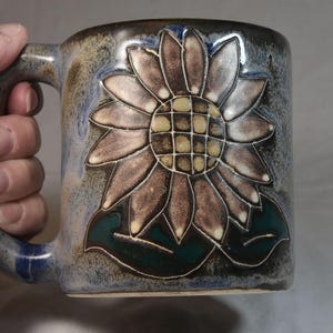 May include: A white ceramic mug with a black handle and the text "But first, coffee" in a handwritten style. The mug is on a white surface. The mug is 4 inches tall.