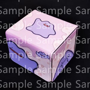 May include: A pink and purple cube-shaped box featuring a cartoon character design. The box has a gradient color scheme and a repeating pattern of the character and floral accents. The box is likely for storage or display.