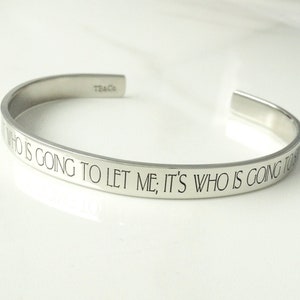 May include: Silver bangle bracelet with the inscription "It's not who is going to let me; it's who is going to stop me."