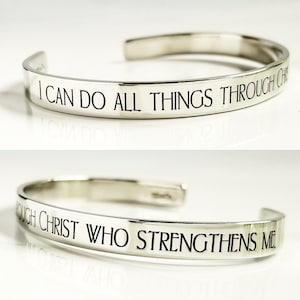 May include: A silver cuff bracelet with the engraved text "I CAN DO ALL THINGS THROUGH CHRIST WHO STRENGTHENS ME." The bracelet has a simple, elegant design and a polished finish.