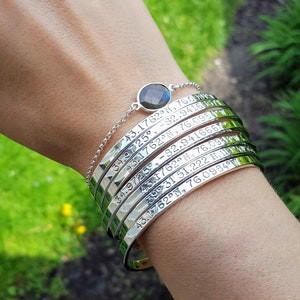 May include: A silver bracelet with multiple bands engraved with coordinates. The bracelet has a dark gray gemstone charm.