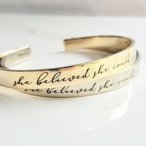 May include: Two gold bracelets with the inscription "She believed she could so she did" on one bracelet and "She believed she could" on the other bracelet.