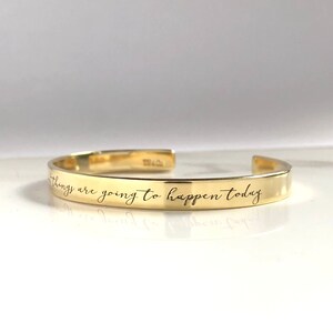 May include: Gold bangle bracelet with the inscription "things are going to happen today" engraved on the outside.