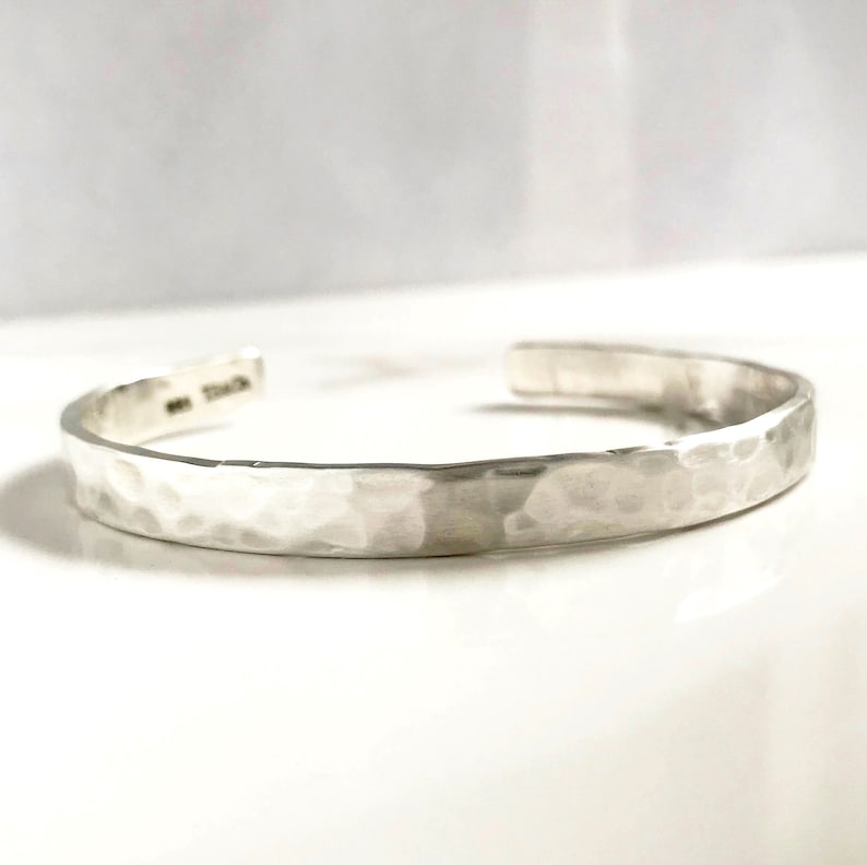 Puede incluir: Un brazalete de plata martillado. El brazalete est&aacute; hecho de un metal grueso y texturizado y tiene un dise&ntilde;o simple y elegante.