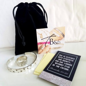 Puede incluir: Un conjunto de dos pulseras de plata con dise&ntilde;os de estrellas. Una pulsera tiene las palabras "Be Still" grabadas. Las pulseras est&aacute;n empaquetadas en una bolsa de terciopelo negro con una peque&ntilde;a tarjeta que dice "Ella est&aacute; vestida de fuerza y dignidad, y se r&iacute;e sin miedo al futuro. Proverbios 31:25".
