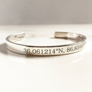 May include: Silver bangle bracelet with engraved coordinates, "36.061214°N, 86.834477°W".