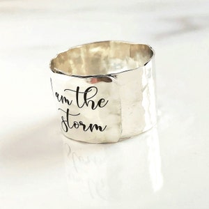 May include: Silver ring with a hammered finish and the words "I am the storm" engraved on the band.