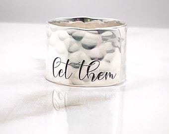 May include: Silver hammered ring with the words "let them" engraved on the band.