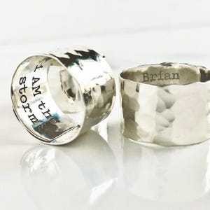 May include: Two silver rings with hammered textures. One ring is engraved with the text "I am the storm". The other ring is engraved with the name "Brian".