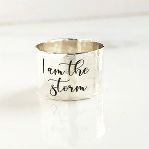 May include: Silver ring with a hammered finish and the inscription "I am the storm" engraved on the band.