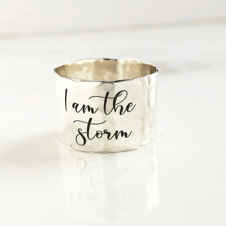 May include: Silver ring with a hammered finish and the inscription "I am the storm" engraved on the band.