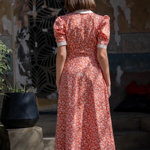 Pode incluir: Vestido vermelho com estampa floral, gola branca e mangas curtas. O vestido tem um corpete ajustado e uma saia rodada, e vai at&eacute; a altura da panturrilha. O vestido &eacute; feito de um tecido leve.