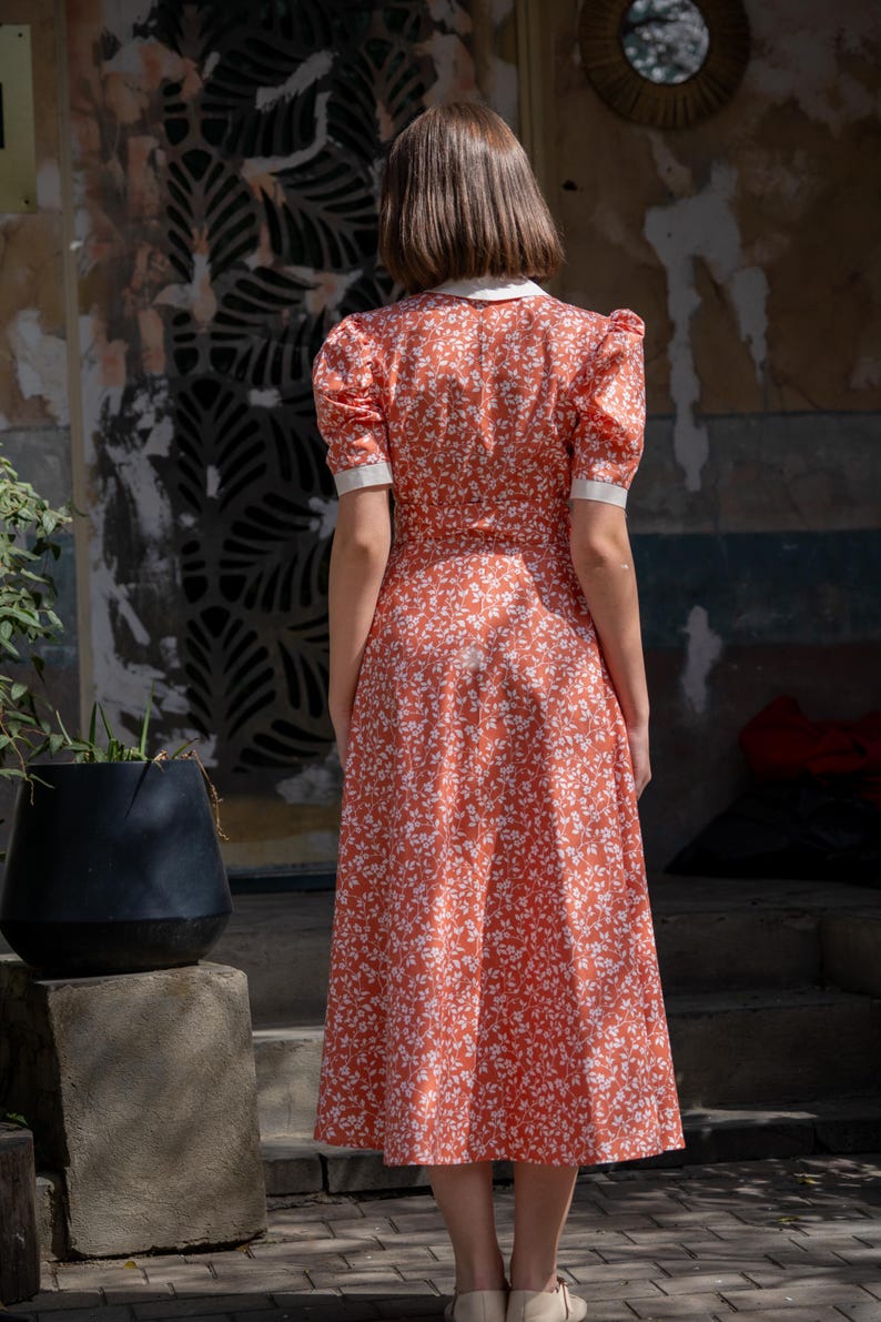 Pode incluir: Vestido vermelho com estampa floral, gola branca e mangas curtas. O vestido tem um corpete ajustado e uma saia rodada, e vai at&eacute; a altura da panturrilha. O vestido &eacute; feito de um tecido leve.