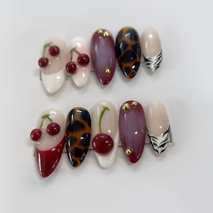 May include: Set of ten false nails with various designs.  The nails feature a cherry design, a leopard print, a zebra print, and a solid color.  The nails are all almond shaped and have a glossy finish.