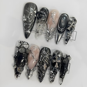 May include: Set of ten black and silver nail tips with various designs, including spiderwebs, crosses, and rhinestones.