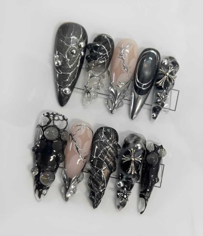 May include: Set of ten black and silver nail tips with various designs, including spiderwebs, crosses, and rhinestones.