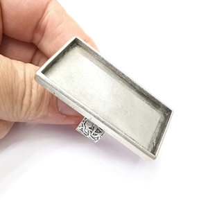 Peut inclure: Plateau de bague rectangulaire en argent avec une surface lisse et plate. Le plateau est conçu pour contenir un petit bijou ou un autre objet décoratif.