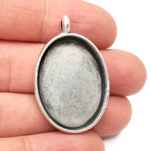 May include: Silver oval pendant with a clear glass insert, perfect for adding a personal touch to jewelry projects.