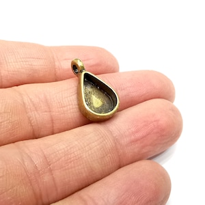 May include: A gold-toned metal pendant with a teardrop-shaped bezel for a cameo or other embellishment. The pendant has a loop at the top for attaching to a chain or cord.