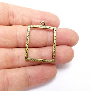 May include: A gold-toned metal frame with a textured surface. The frame is square shaped and has a loop at the top for hanging.