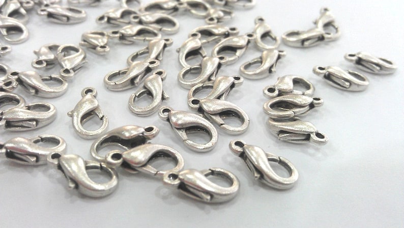 May include: A large group of silver-toned lobster claw clasps, a type of jewelry finding used for attaching chains or cords to jewelry pieces.