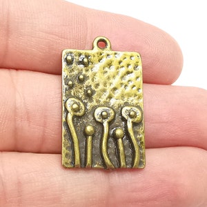 Könnte beinhalten: Ein goldfarbener Metallanhänger mit rechteckiger Form und einer strukturierten Oberfläche. Der Anhänger zeigt ein Design aus fünf stilisierten Blumen mit abgerundeten Spitzen und Stielen.