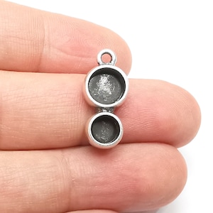 May include: Silver pendant with two round, empty, bezel settings. The pendant has a loop at the top for attaching to a chain or cord.