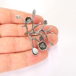 May include: Silver ring with a tree branch design, featuring multiple round settings and a single flower setting. The ring is shown on a hand.
