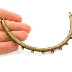 May include: A gold-toned metal jewelry finding with a curved shape and multiple small loops. The finding is designed for attaching jewelry components.