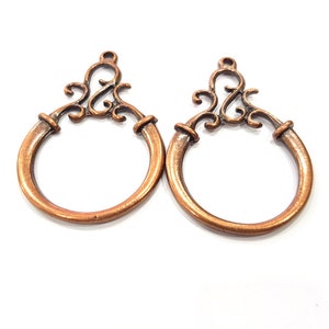 May include: Two copper-colored metal rings with ornate scrollwork designs. The rings are about 2 inches in diameter and have a smooth, polished finish.