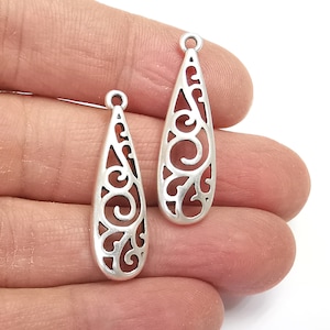 May include: Two silver filigree teardrop shaped pendant charms with a swirl design.