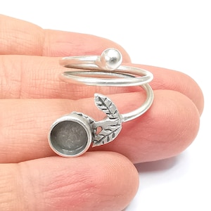 Può includere: Anello d'argento con un design a spirale e una montatura rotonda. L'anello ha un design a foglia su un lato.